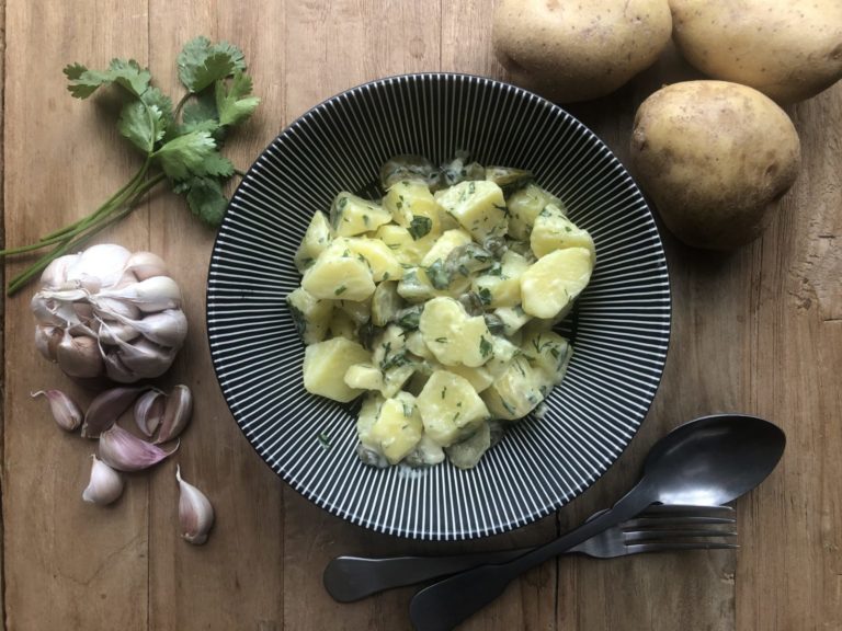 Schwarze Schale mit Kartoffel-Apfel-Salat und frischen Gartenkräutern