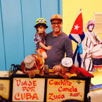Papa Corazón in Kuba mit seinem Sohn hinter einem kubanischen Essensstand mit buntem Hintergrund mit kubanischer Flagge