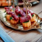 Schinken-Melonen-Spieße mit Minze auf goldenem, blätterförmigen Tablett für Fingerfoodbüffet
