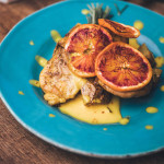Hühnerbrust mit Safran-Blutorangen-Salsa auf türkisem Teller angerichtet mit kleinen gelben Saußenspritzern verteilt als Idee für eine Hauptspeise Familienfeier