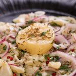 Handkäse mit roten Zwiebeln und Kümmel bestreut auf schwarzem Teller - Idee für deutsches Büffet