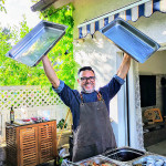 Papa Corazón Koch freut sich bei Catering Gartenparty in Bad Homburg, dass er grillen kann und lacht, während er zwei Behälter hoch hält