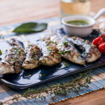 Gegrillte Sardinen auf dunkelblauem Teller mit Olivenöl und Tomate dekoriert als Idee für mediterranes oder Grill-Menü