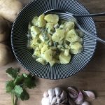Schwarze Schale mit Kartoffel-Apfel-Salat und frischen Gartenkräutern